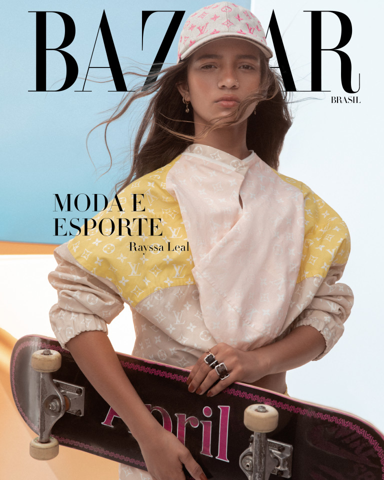 A skatista Rayssa Leal usa look Louis Vuitton (boné com monograma da marca em rosa, jaqueta com o monograma em branco e fundo rosa e amarelo e anéis com fivelas), segurando skate preto com a palavra April (abril, em português) estampada embaixo